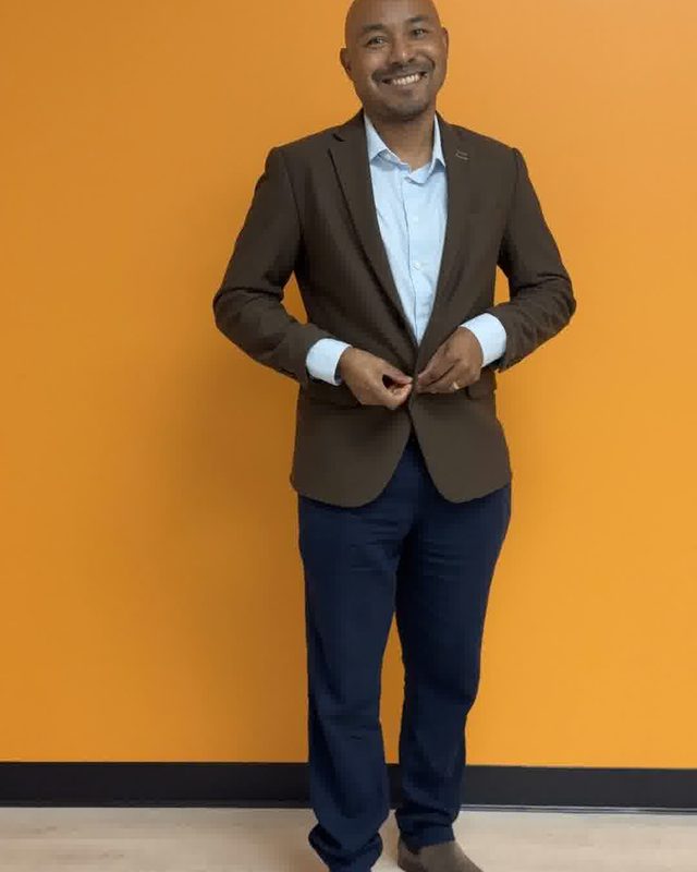 Still from a reel: Martial standing against an orange wall in a blazer