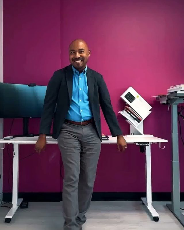 Still from a reel: Martial leaning against a desk in front of a magenta wall